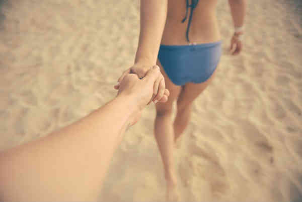 woman leading man by the hand on the beach