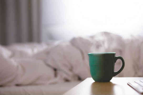 a coffe cup next to a messy bed