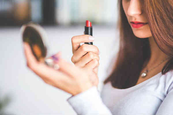 woman looking in mirror holding lipstick