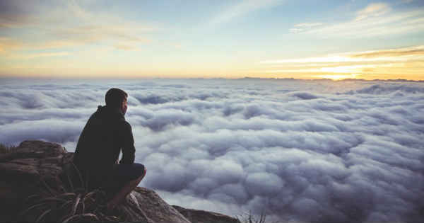 man sitting on a cliff overlooking clouds