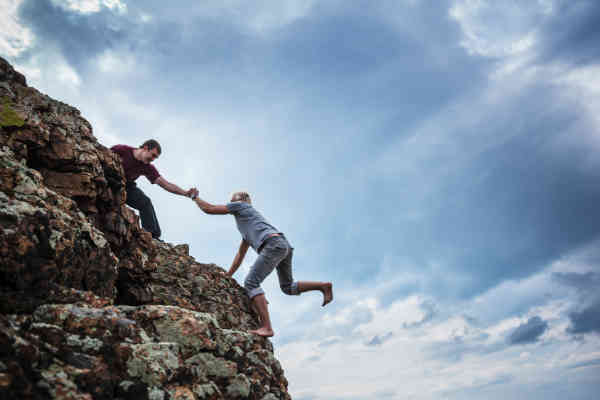 man helping woman climb a mountain