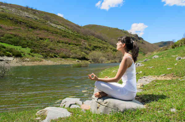 woman meditating next to a river
