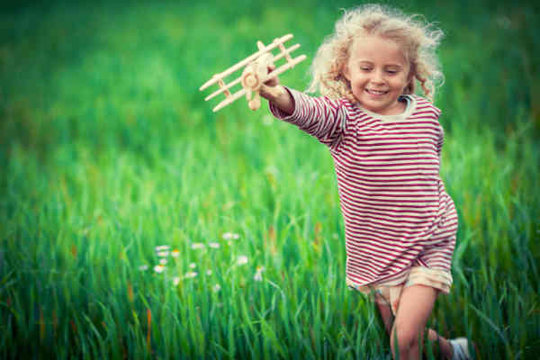 child playing with an airplane in a lush field